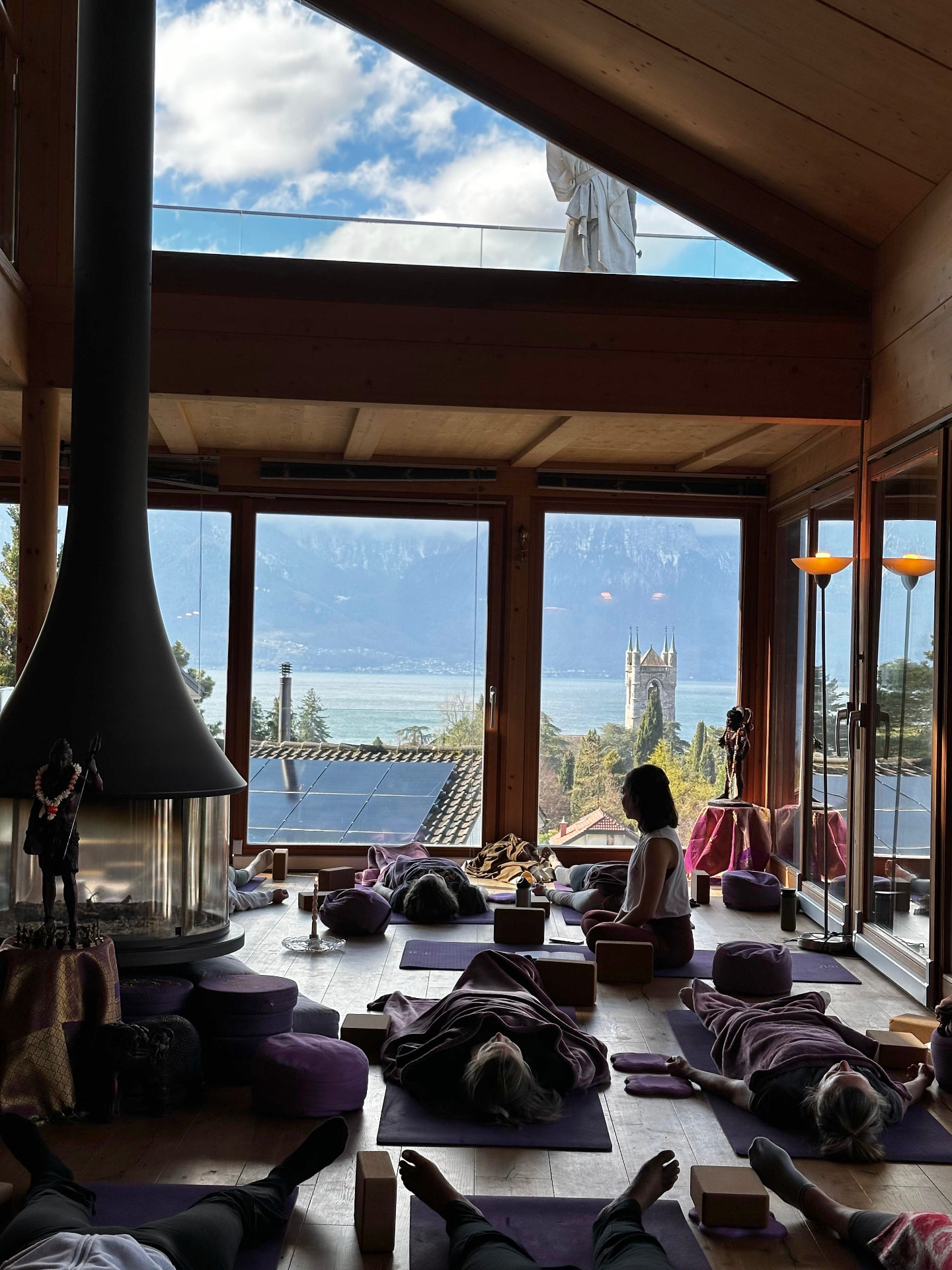 Séance de yoga dans une salle aux grandes baies vitrées, lac et montagnes à l'horizon