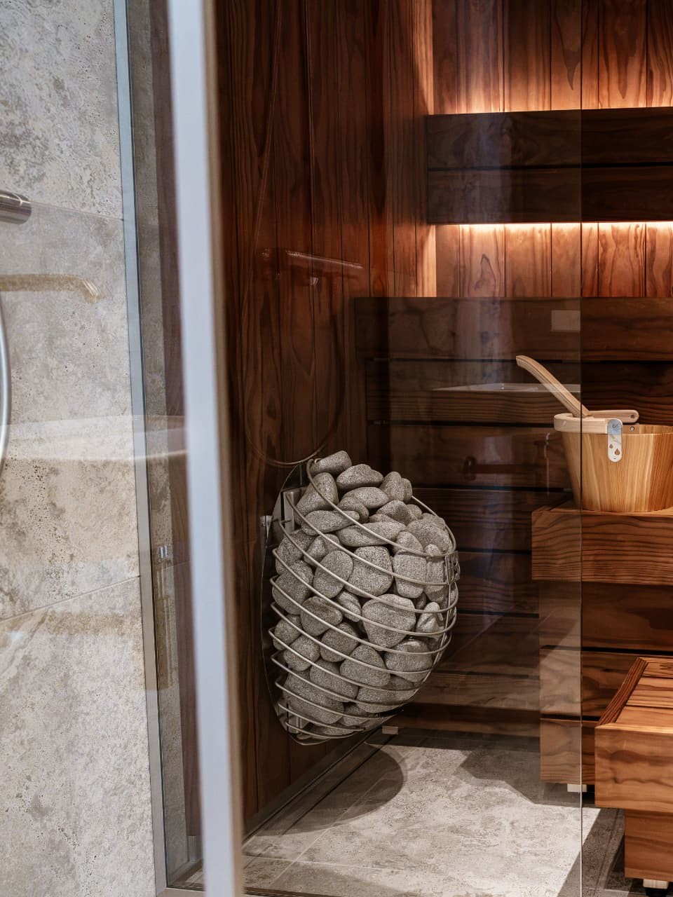 Sauna en bois clair, poêle à pierres et lueur dorée, vu à travers la porte vitrée