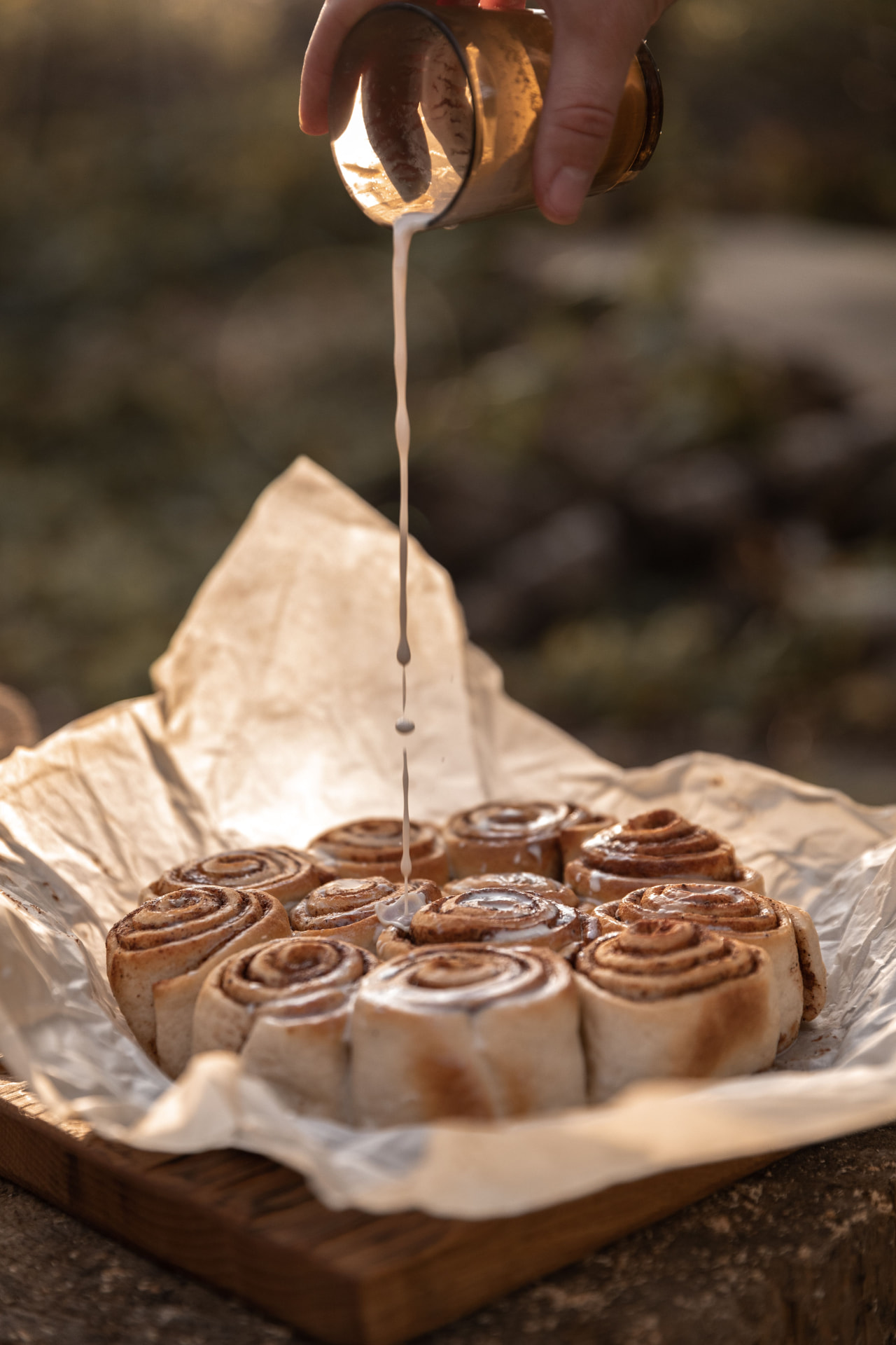 Glaçage versé sur des cinnamon rolls encore chauds, en lumière dorée de fin de journée