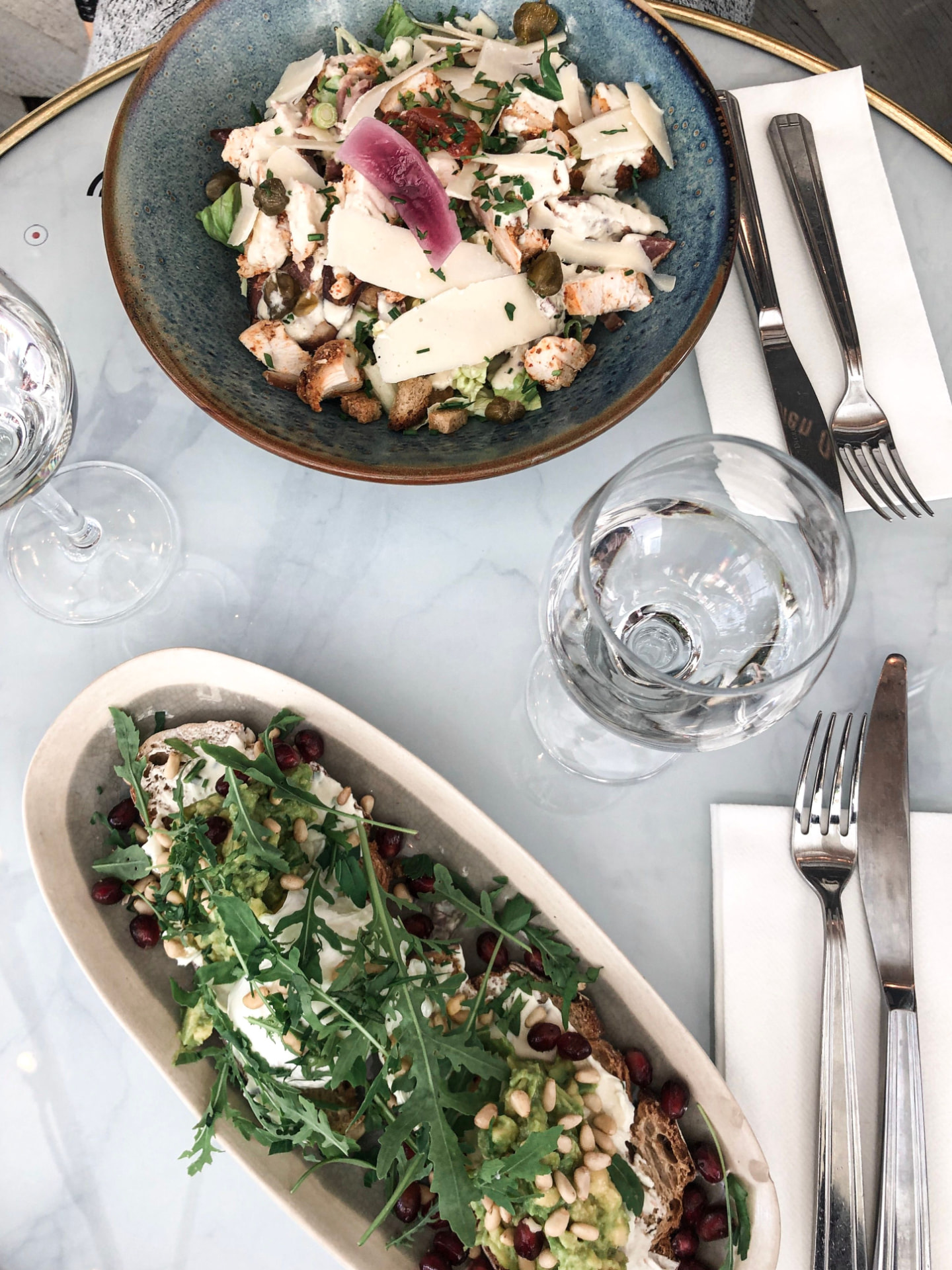 Bowl de salade César au poulet et tartine à l'avocat, roquette et pignons, sur une table en marbre