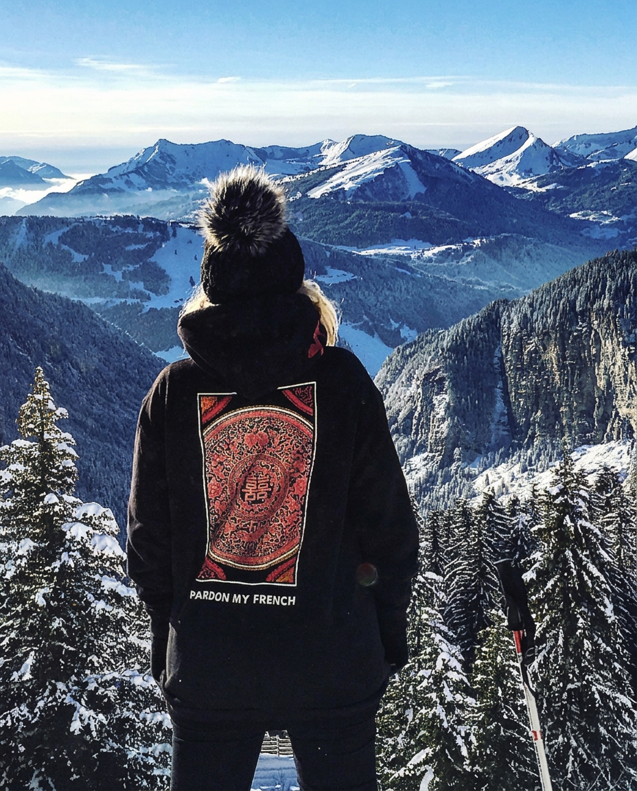 Personne de dos en doudoune noire, face à un panorama de sommets enneigés et de forêts givrées